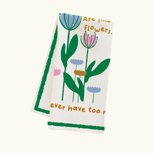 A white cotton dish towel with a floral pattern and a text phrase 'Friends are like flowers you can never have too many' 

