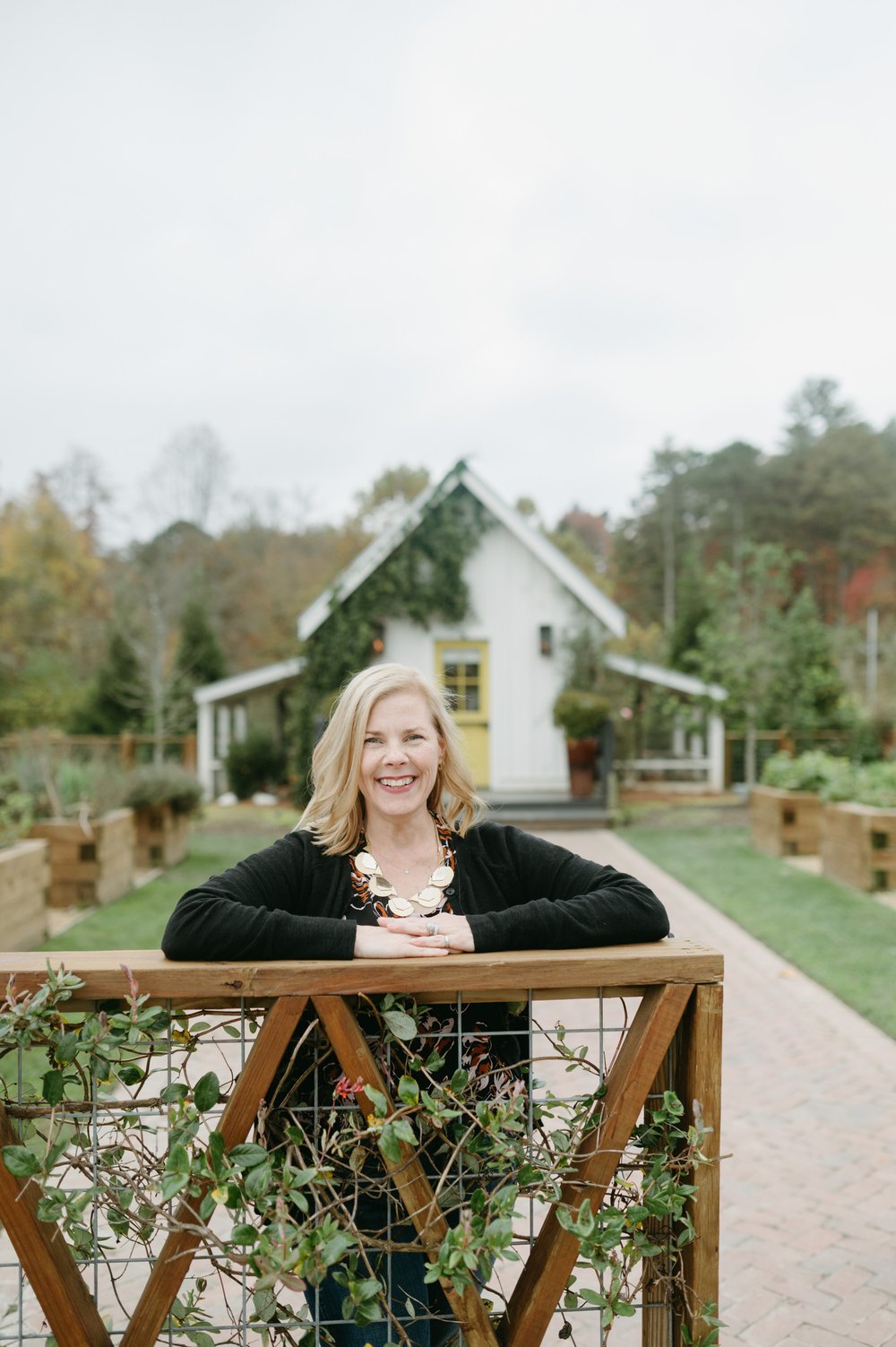 tracey wirth standing in front of small white shed with yellow door.