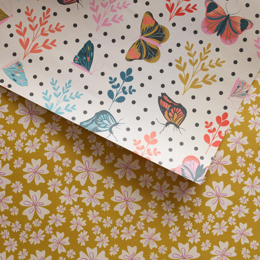 double sided Wrapping paper with a vintage floral pattern on a yellow background on one side, and a pattern of illustrated butterflies on a polka dot background on the reverse.

